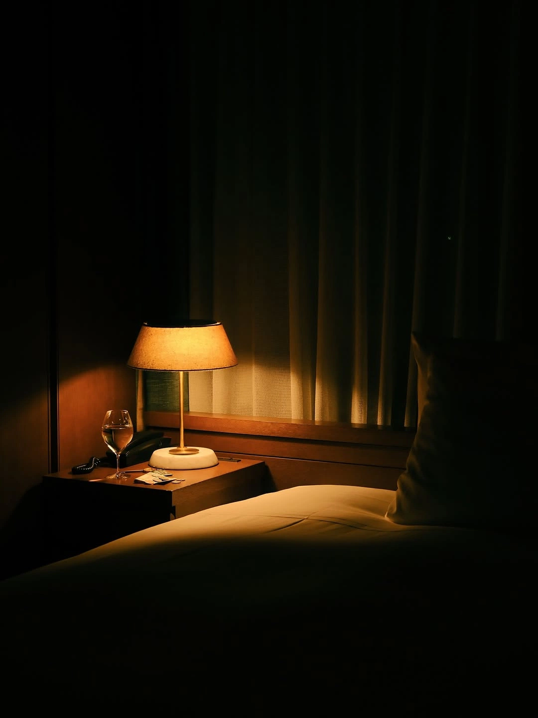 Quiet dark bedroom with a single warm bedside lamp at night