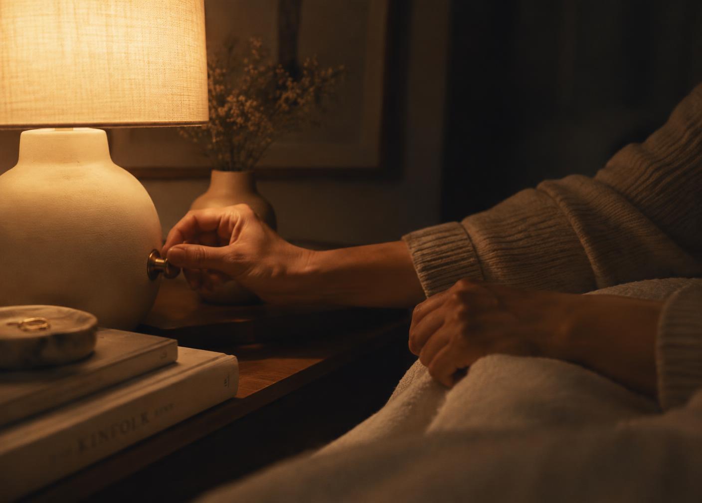 A hand dimming a warm bedside lamp at night